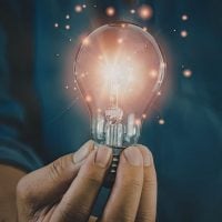 A hand holding a glowing light bulb, sparks floating around, symbolizing a bright idea or innovation.