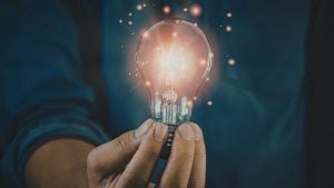 A hand holding a glowing light bulb, sparks floating around, symbolizing a bright idea or innovation.