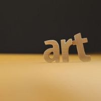art 1 - fundsforNGOs Wooden letters spell 'art' on a warm yellow surface with a dark background, emphasizing art concept.