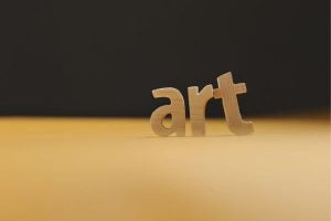 Wooden letters spell 'art' on a warm yellow surface with a dark background, emphasizing art concept.