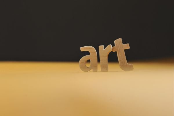 Wooden letters spell 'art' on a warm yellow surface with a dark background, emphasizing art concept.