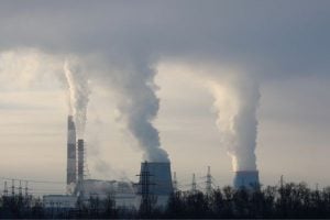 Industrial power plant with tall smokestacks releasing white steam into a cloudy sky.