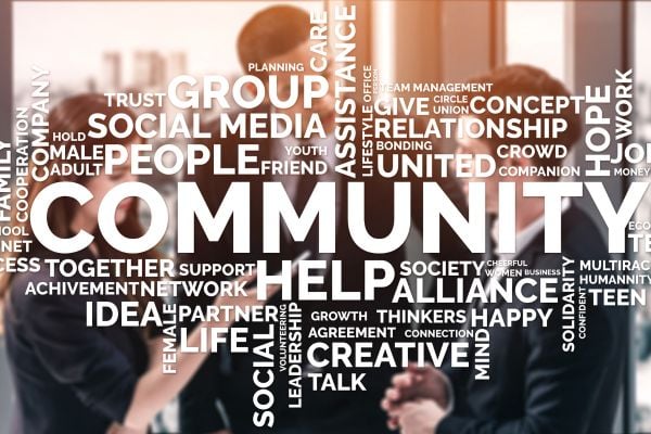community - fundsforNGOs Group of professionals in a meeting with a large word-cloud emphasizing community, collaboration, and helping.