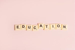Scrabble tiles spell 'EDUCATION' on a soft pink background.