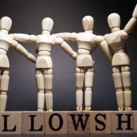 education and sports for children 1 - fundsforNGOs Wooden artist mannequins stand in a row with arms linked, over blocks that spell FELLOWSHIP, symbolizing unity.