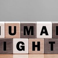 Wooden letter blocks spell 'HUMAN RIGHTS' on a wooden table, arranged in two rows.