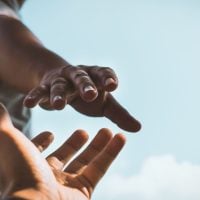 Two hands reaching toward each other against a bright blue sky, suggesting connection or support.