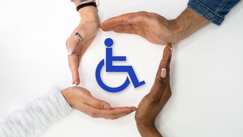 education and sports for children 3 - fundsforNGOs Diversity of hands forming a protective circle around a blue wheelchair accessibility symbol, conveying support and inclusion for people with disabilities.