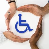 Diversity of hands forming a protective circle around a blue wheelchair accessibility symbol, conveying support and inclusion for people with disabilities.