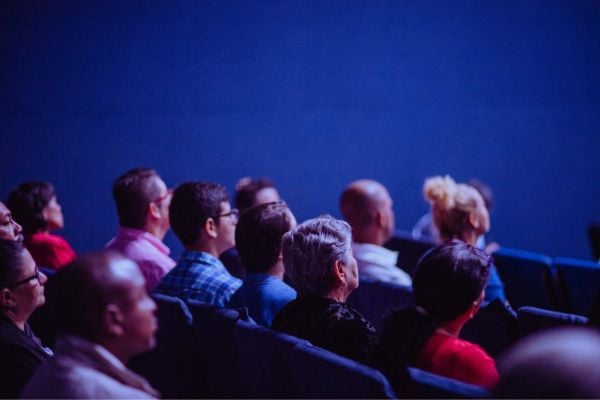 film - fundsforNGOs Audience seated in rows facing a stage in a dark blue-lit theater or conference space.