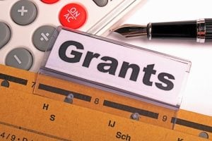 Close-up of a sign reading 'Grants' atop a ruler with a fountain pen and calculator nearby, suggesting budgeting or funding.