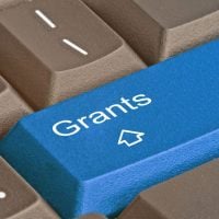 grant - fundsforNGOs Blue keyboard key labeled 'Grants' with a white graduation cap icon, among brown keys.