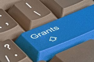 Blue keyboard key labeled 'Grants' with a white graduation cap icon, among brown keys.