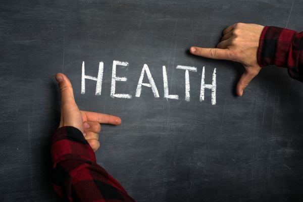 Hands frame the word HEALTH written in chalk on a dark chalkboard edge.