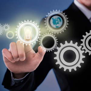 Person in a suit touches a glowing lightbulb inside a gear, symbolizing innovation and global collaboration.