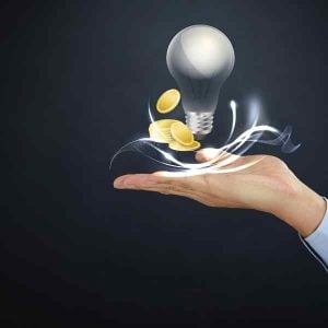 Hand holding a glowing light bulb with coins around it, symbolizing funding an idea or startup investment.