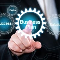 BUSINESS 1 - fundsforNGOs Hand pointing to a glowing 'Business Plan' gear, surrounded by gears labeled 'Success', 'Ideas', 'Strategy', 'Solution', and 'Teamwork'.