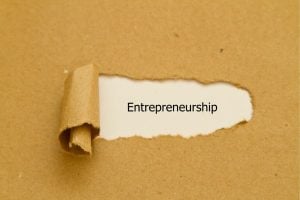 Torn white strip reveals the word Entrepreneurship on a brown kraft background.