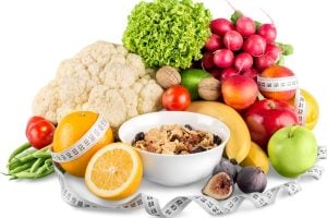 Colorful assortment of fruits and vegetables surrounding a bowl of granola, with a measuring tape draped around—symbolizing healthy eating and dieting.