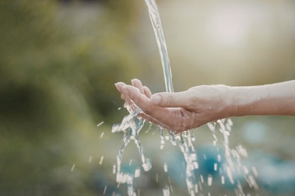 Hands cupped under a stream of running water from a faucet or fountain, droplets visible in midair.