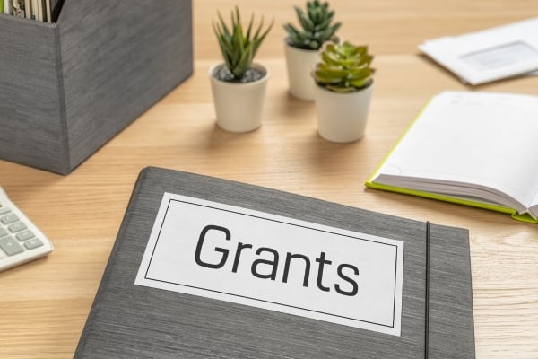 Binder labeled Grants on a wooden desk with small potted plants, an open notebook, and a calculator nearby.