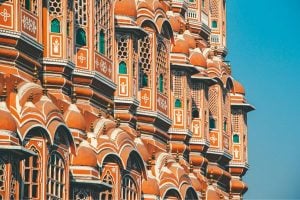 Ornate orange palace facade with repeating arched windows and white detailing against a clear blue sky sincely bright light.