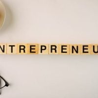 Innovators and Entrepreneurs - fundsforNGOs Wooden letter tiles spell 'ENTREPRENEUR' on a light desk with a coffee cup nearby.