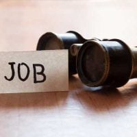 Jobs for Youth 1 - fundsforNGOs Card labeled JOB beside a small telescope on a wooden surface, suggesting a job search concept.