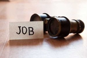 Card labeled JOB beside a small telescope on a wooden surface, suggesting a job search concept.