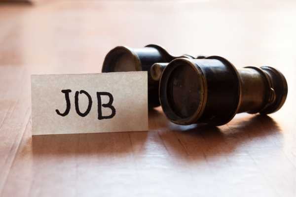 Card labeled JOB beside a small telescope on a wooden surface, suggesting a job search concept.