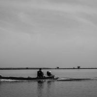 Livelihoods 1 - fundsforNGOs Two people in a small motorboat gliding across calm water with a distant shoreline visible in the background.