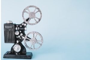 Vintage film projector with two metal reels on a black base against a light blue background, ready to project film.