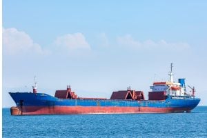 Blue cargo ship with red hull sections sailing on calm blue sea under a clear sky.