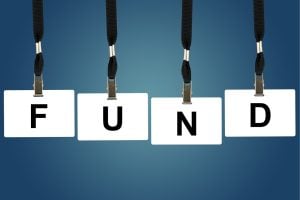 Four white letter tiles hanging spell the word FUND against a blue gradient background, symbolizing funding or finance.