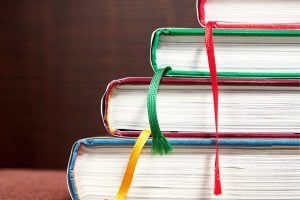 Stack of colorful hardcover books stacked on a surface with ribbon bookmarks hanging from the edges.