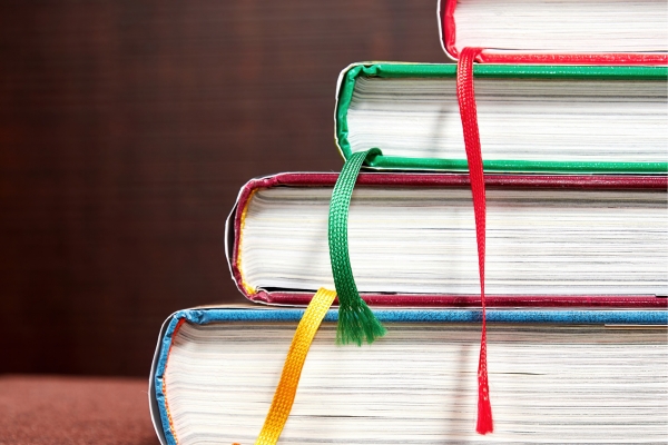 Stack of colorful hardcover books stacked on a surface with ribbon bookmarks hanging from the edges.