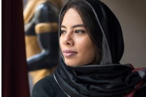 Woman wearing a black hijab gazing thoughtfully out a window.