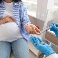 Maternal - fundsforNGOs Pregnant woman seated with hand on belly as a clinician in blue gloves administers a vaccine in her upper arm.