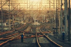 Rail yard with many parallel and intersecting train tracks under overhead electric lines at sunset.