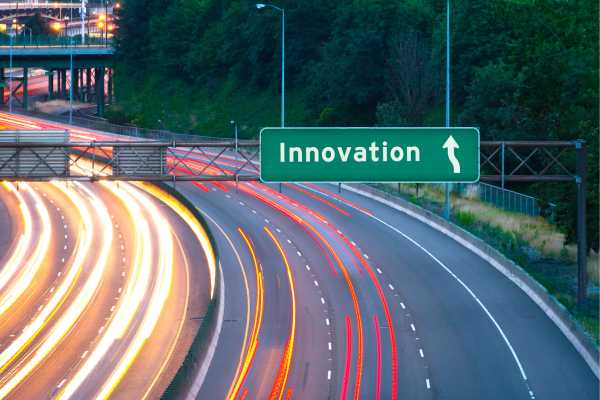 Road Transport and Innovation - fundsforNGOs Green highway sign reading 'Innovation' with an upward arrow over a curved multi-lane highway at dusk, showing light trails from passing cars toward the direction of innovation.