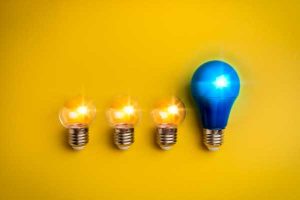 Four light bulbs in a row on a yellow background; three small incandescent bulbs lit and one larger blue bulb lit on the right.