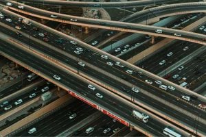 Bird's-eye view of a multi-level highway interchange with many lanes and vehicles in motion, showing complex ramps and overpasses in urban traffic.