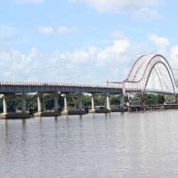 Waterways Infrastructure - fundsforNGOs Long arched bridge spanning a calm river under a blue, partly cloudy sky with distant hills in the background.