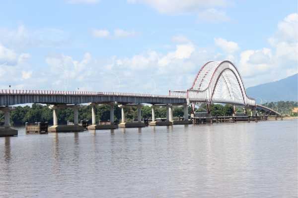 Waterways Infrastructure - fundsforNGOs Long arched bridge spanning a calm river under a blue, partly cloudy sky with distant hills in the background.