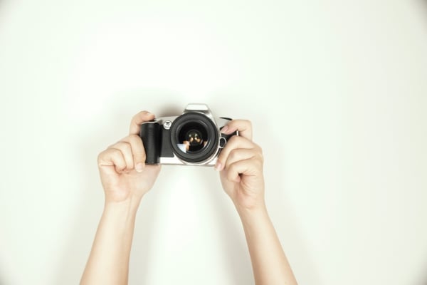 Person holding a silver camera up to take a photo, hands visible against a light background.
