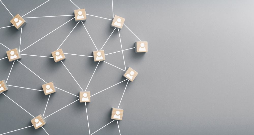community 3 - fundsforNGOs Wooden blocks with user icons connected by white lines forming a social/network graph on a gray background, representing connectivity between people.