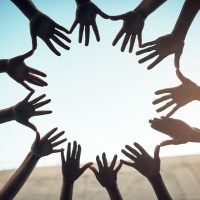 community 4 - fundsforNGOs People join hands in a circle against a blue sky, symbolizing teamwork and unity.