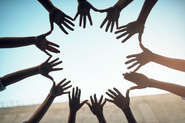 community 4 - fundsforNGOs People join hands in a circle against a blue sky, symbolizing teamwork and unity.