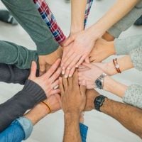 community 7 - fundsforNGOs Group of diverse hands stacked together in the center, representing teamwork and unity.