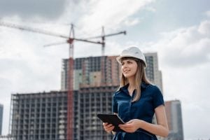 Construction site scene with a worker in a hard hat holding a tablet, surveying progress.